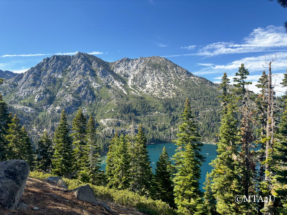 Mountain and forest view from Inspiration Point at South Lake Tahoe, featuring rugged peaks and a clear blue sky above a dense forest and Emerald Bay in the distance.