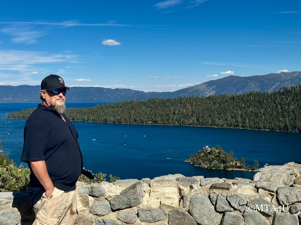 Photo of Illya from MTA4U standing at the Vikingsholm Castle parking lot overlook, with a picturesque view of Emerald Bay and the surrrounding forest in the background.