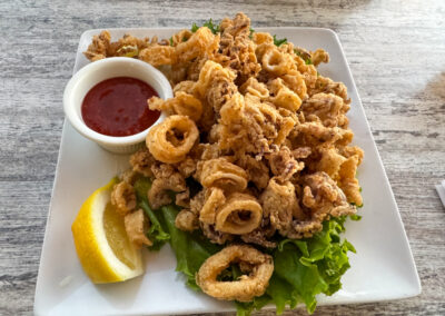 A plate of crispy fried calamari served with a dipping sauce, lemon wedges, and garnish.