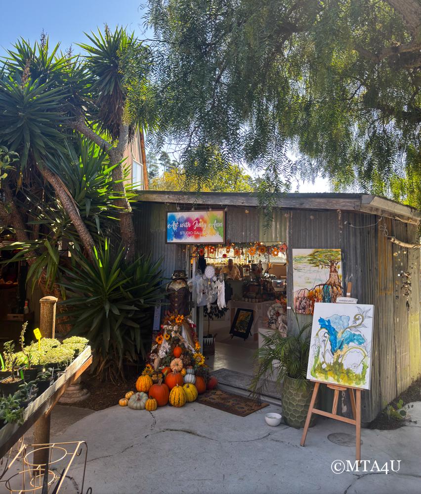 The entrance of Art with Judy Ann studio gallery in Cambria's East Village, with colorful paintings and fall-themed decor.