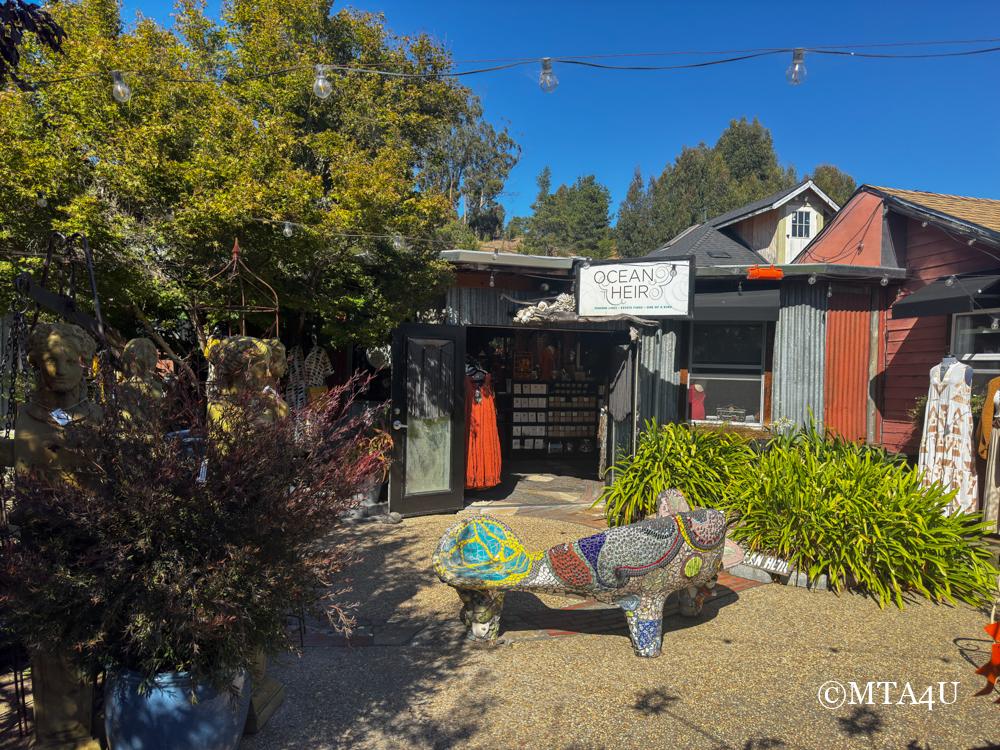 The exterior of Ocean Heir, a boutique shop in Cambria's East Village, featuring colorful mosaic bench and outdoor decor.