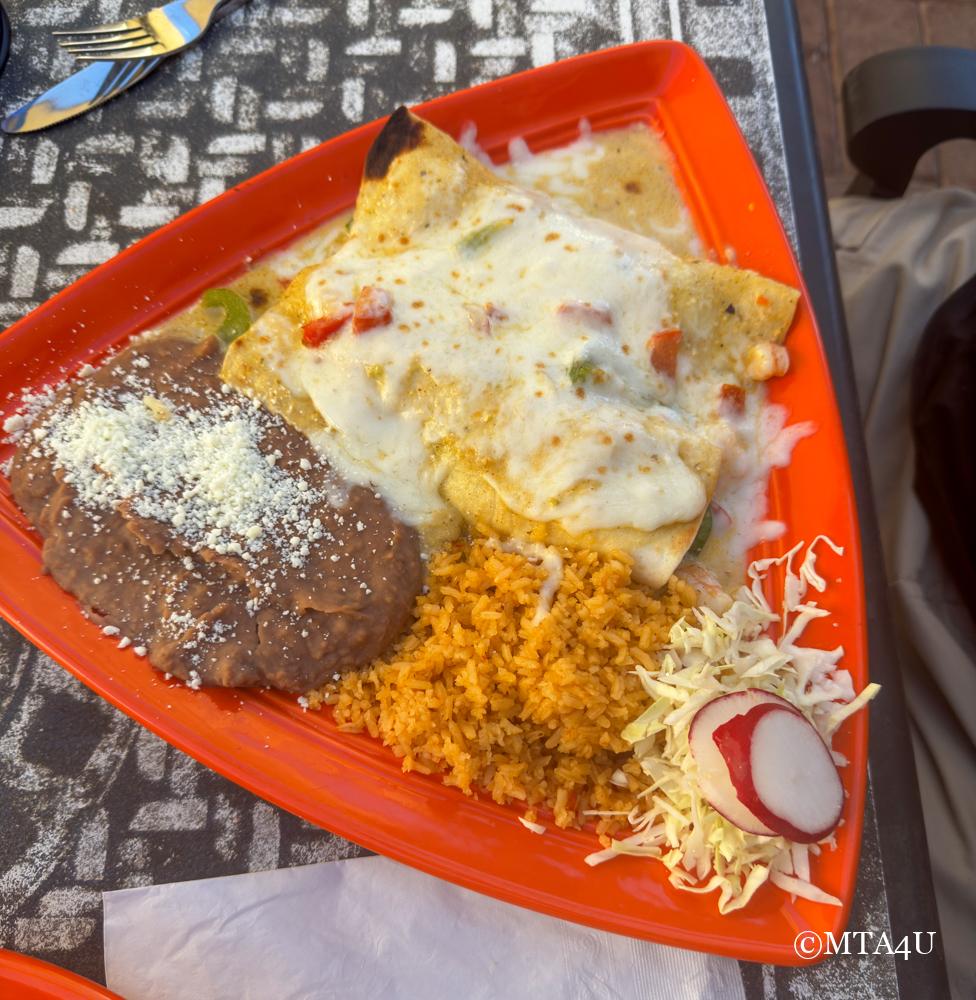 A plate of Baja Shrimp Enchiladas topped with melted cheese, serve with refried beans, Mexican rice, and a side of cabbage slaw at Las Cambritas in Cambria, California.