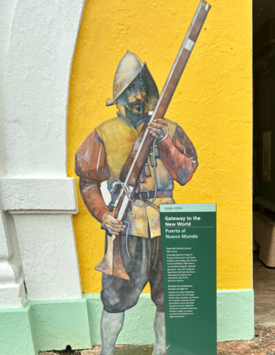 Mural of Spanish Infantryman holding a musket at El Morro fortress in San Juan, Puerto Rico, with informational plaque beside it.