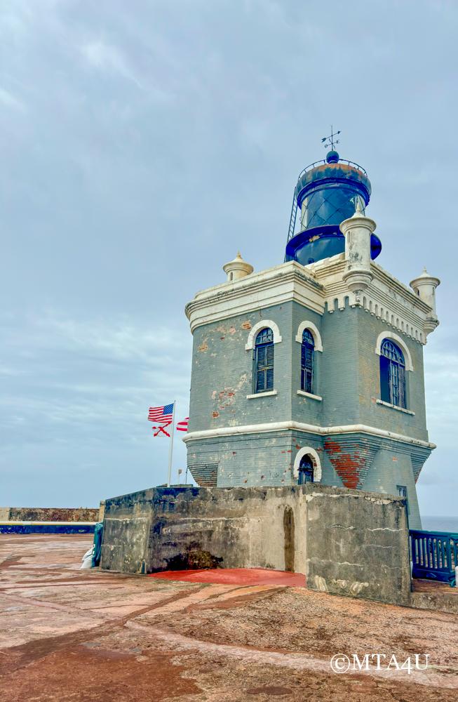 The historic lighthouse at El Morro fortress in San Juan, Puerto Rico, standing against a cloudy sky with flags nearby.