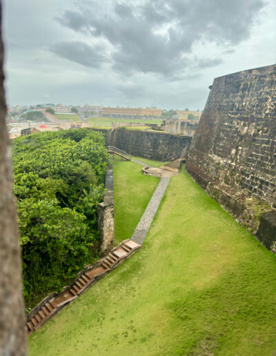 View of green lawns and stone walls within El Morro fortress in San Juan, Puerto Rico, with cloudy skies above.