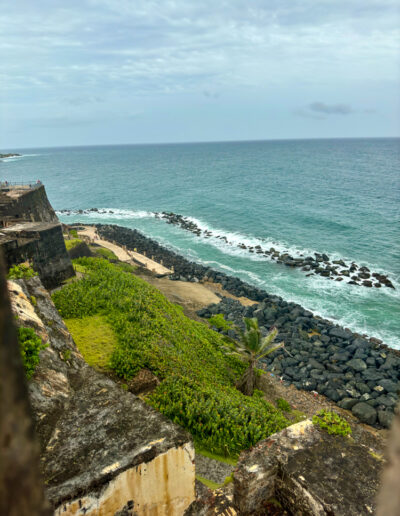 View from El Morro fortress in San Juan, Puerto Rico, showing the Atlantic Ocean, greenery, and rocky coastline.