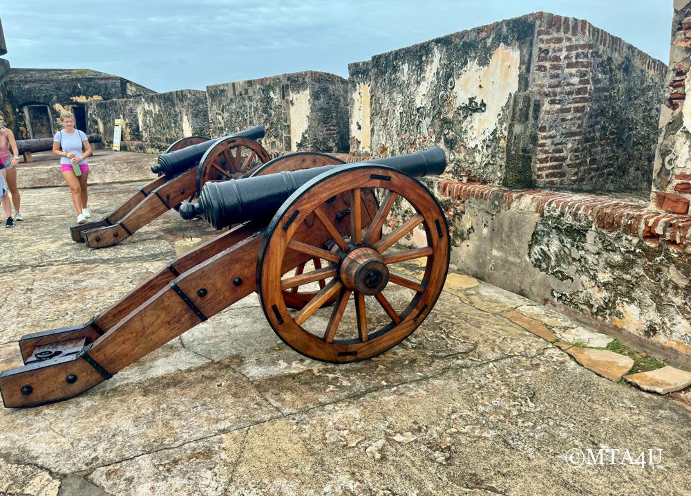 Historic wooden cannons at El Morro fortress in San Juan, Puerto Rico, with weathered walls in the background.