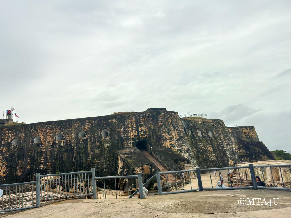 Historic stone walls of El Morro fortress in San Juan, Puerto Rico, with observation platforms and small windows.