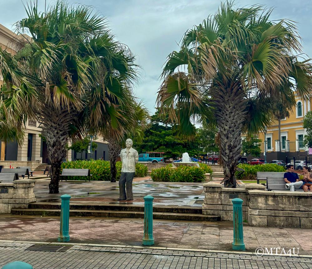 Statue of Don Ricardo Alegria Gallardo in Plaza del Cuartel, San Juan, Puerto Rico, with palm trees and benches in the background.