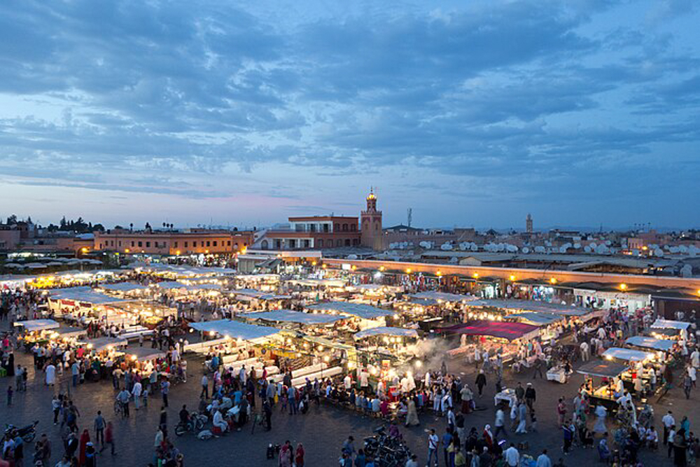 Jemaa el-Fnaa Square in Marrakech, Morocco, bustling with market stalls, lights, and activity under a vibrant sky.