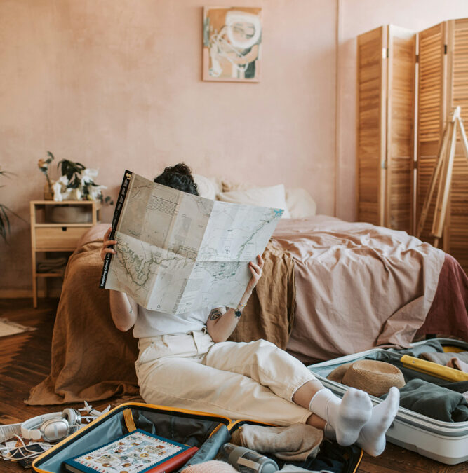 Person sitting on the floor planning travel with a map and open suitcase, representing the freedom of becoming a travel advisor in 2025.
