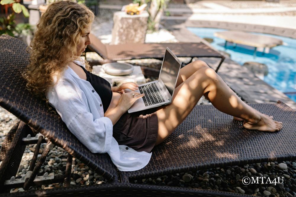 Woman working remotely on a laptop by the pool – building a travel business from anywhere.