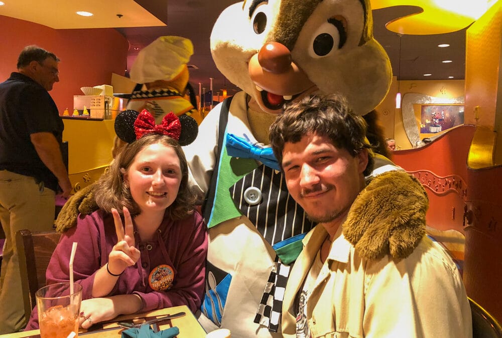 Family enjoying character dining at Disney – child and adult pose with Chip in chef attire during a meal.