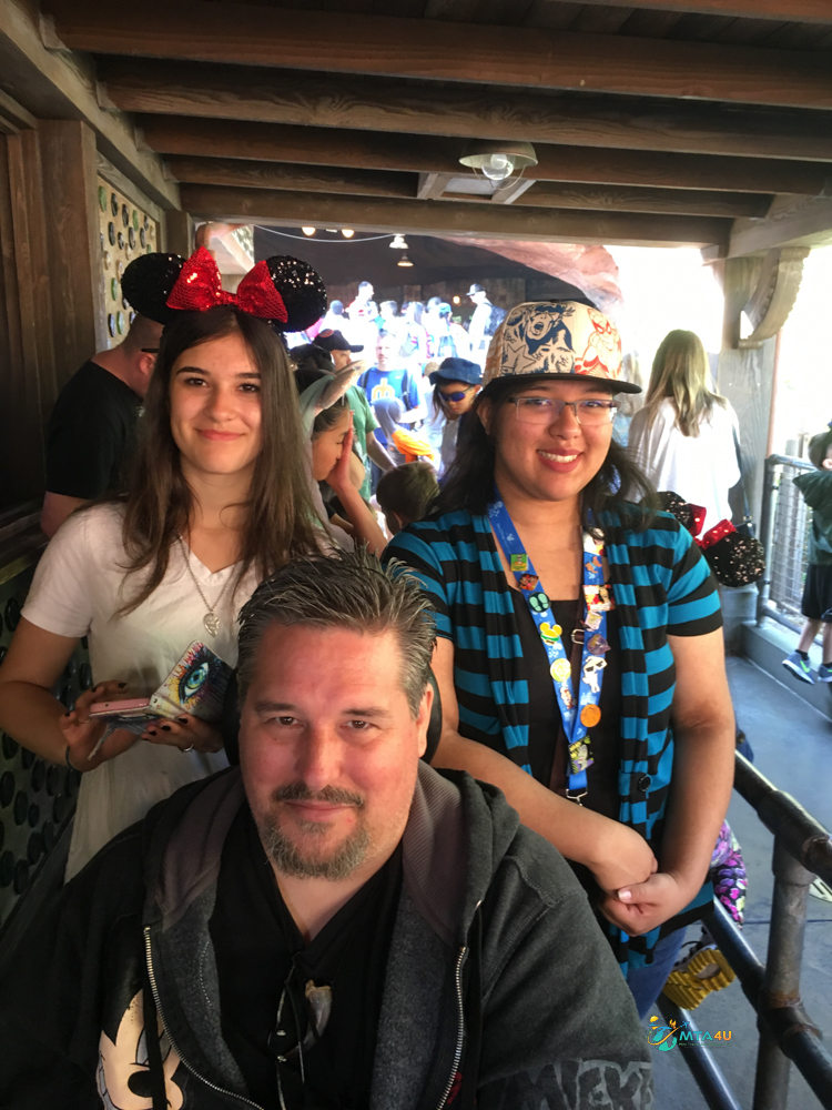 Staying together while navigating lines is easier when your group knows what to expect with scooter rentals. Family group standing in a Disneyland ride queue with a mobility scooter, demonstrating the real-life value of scooter rentals for Disneyland.
