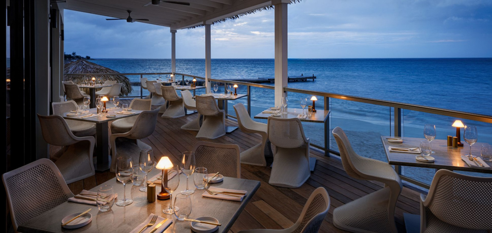Oceanfront Dining at Sandals South Coast Outdoor dining setup at Sandals South Coast with tables overlooking the beach at dusk.