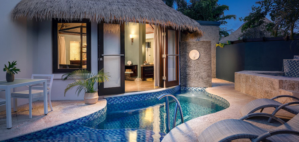 Private Plunge Pool Suite at Sandals A private plunge pool outside a Sandals suite at dusk, featuring a thatched roof and patio furniture.