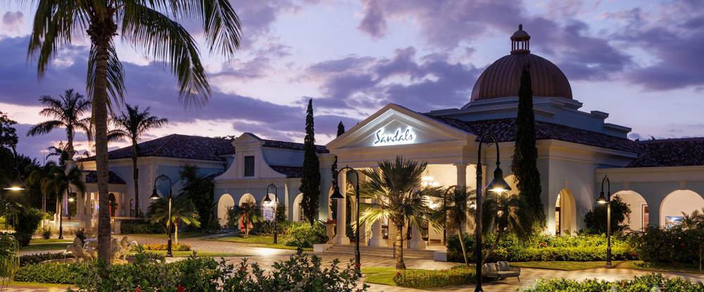 Elegant Entrance at Twilight The grand entrance of Sandals South Coast glows at twilight, surrounded by lush landscaping and illuminated palm-lined pathways.