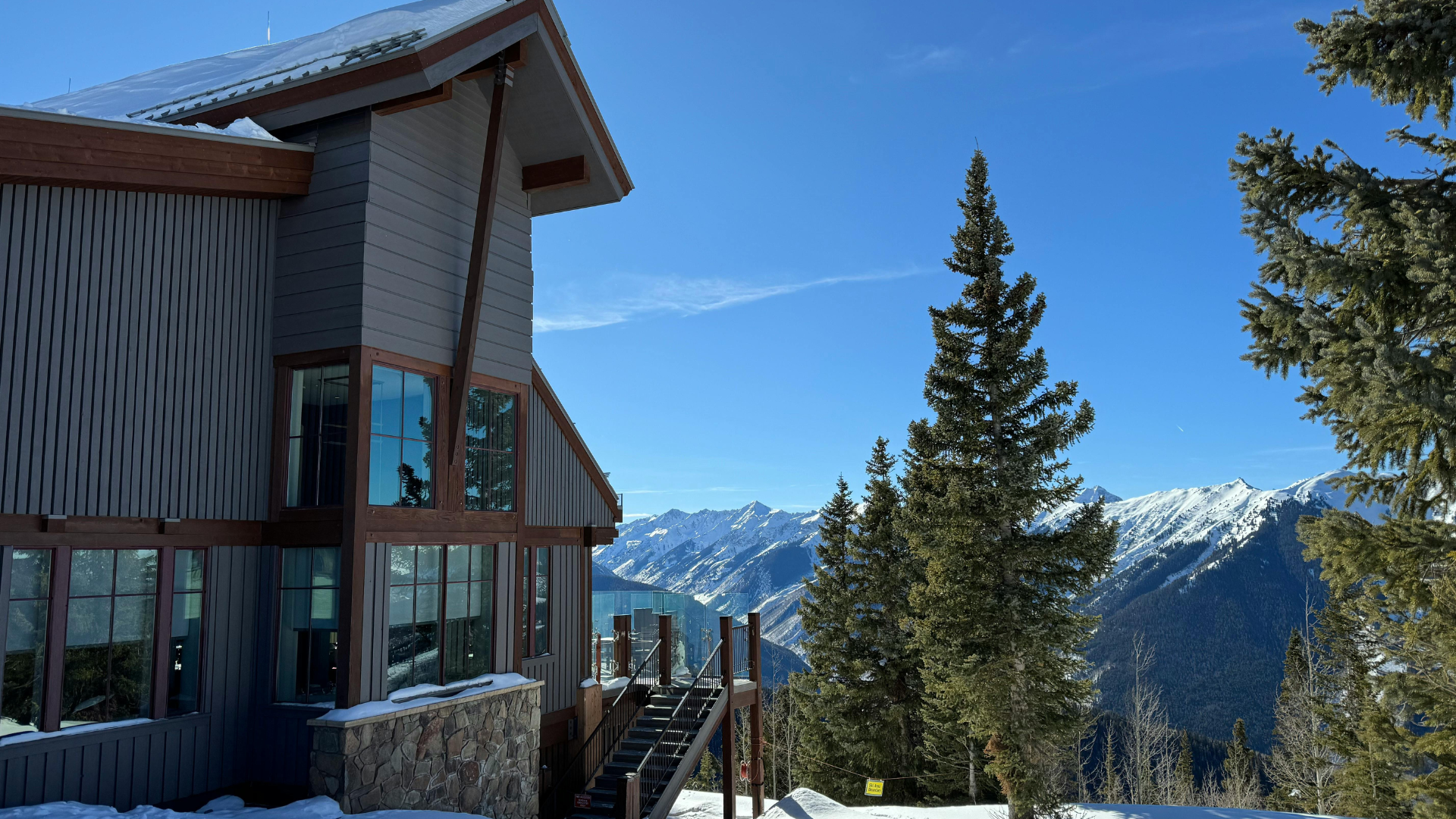 Modern mountain lodge in Aspen, Colorado overlooking snow-covered peaks and evergreen trees on a clear winter day.