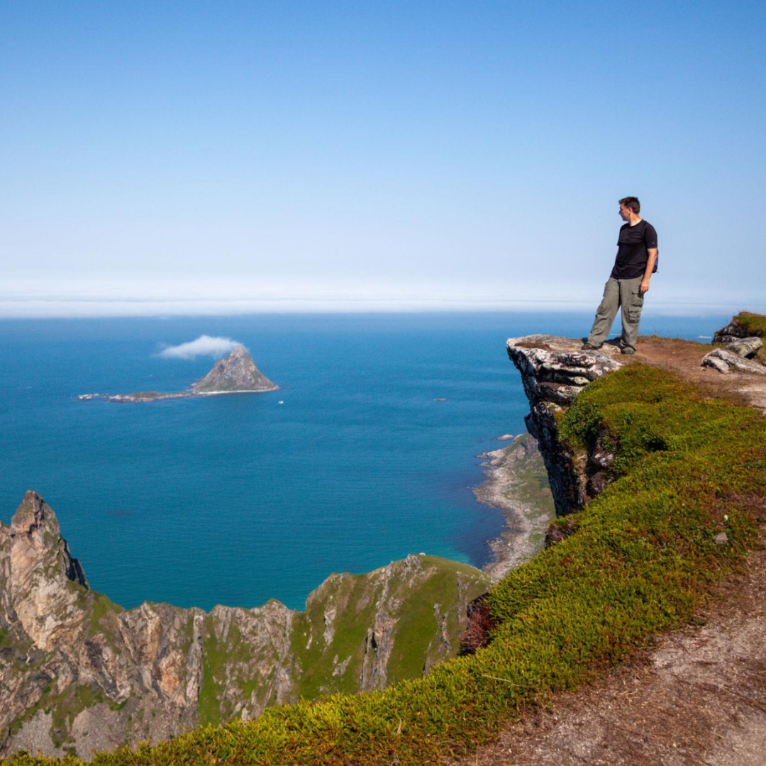Traveler standing on a cliff overlooking the ocean and rugged coastline at a scenic viewpoint.