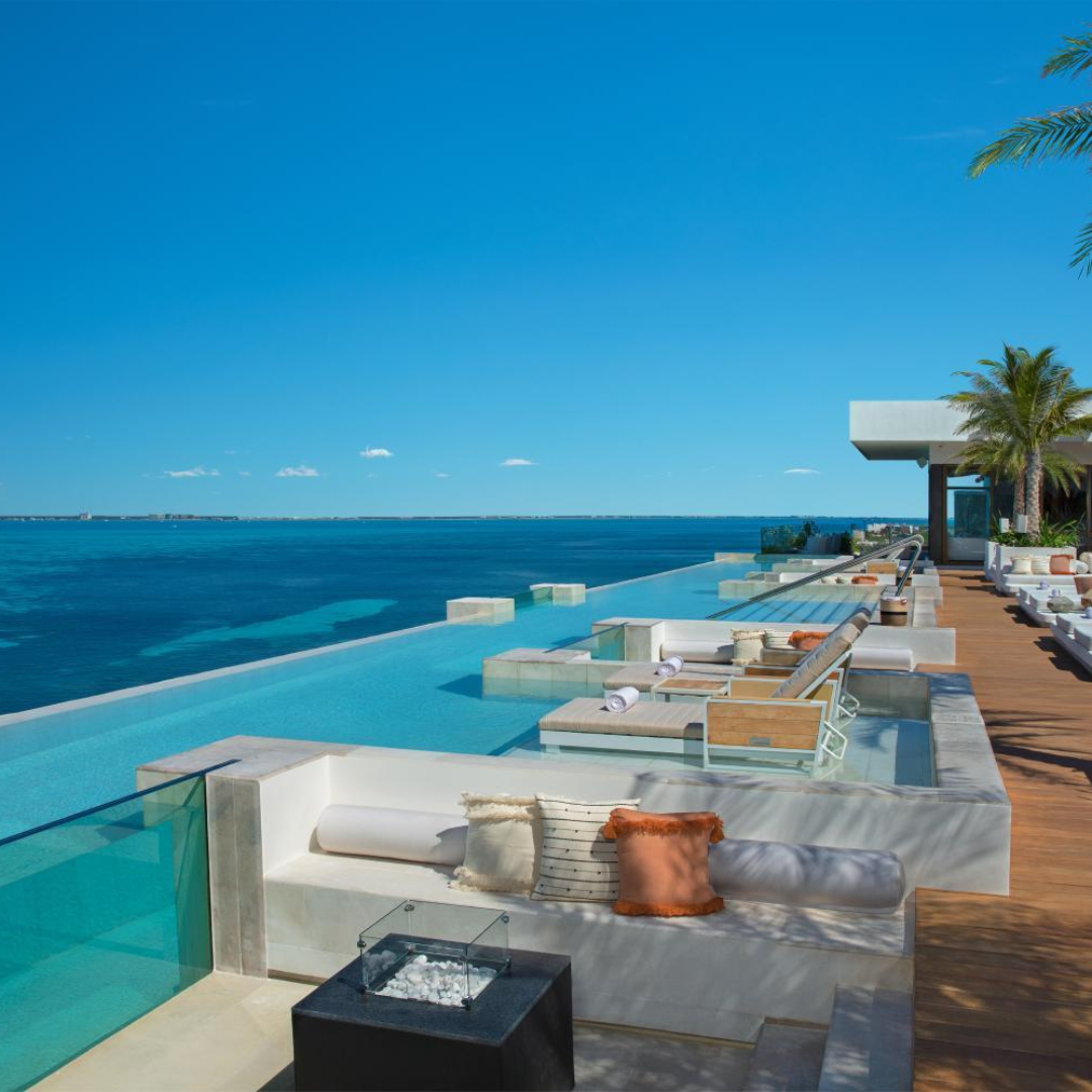 Luxury resort infinity pool overlooking the ocean with lounge seating and palm trees.