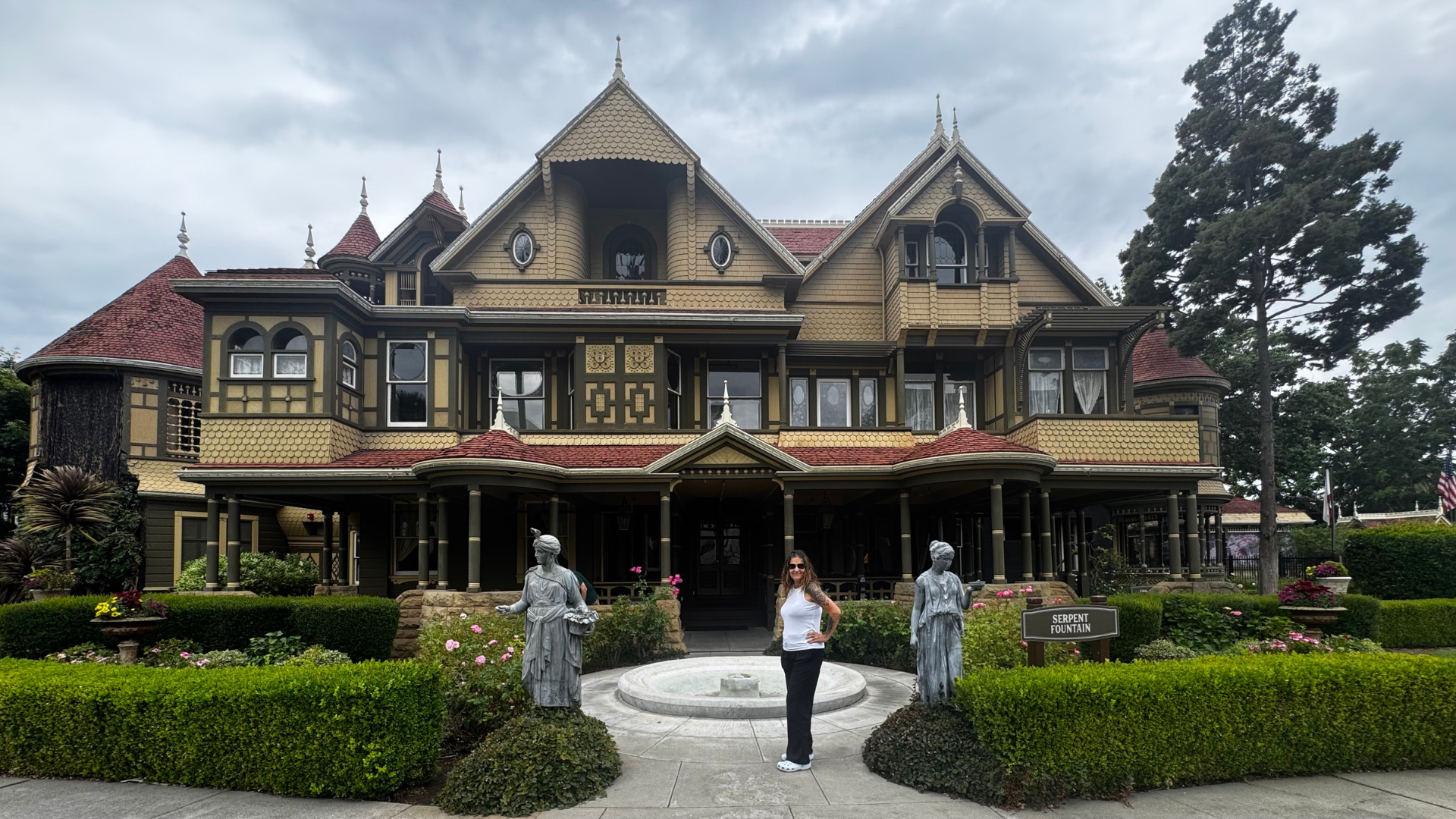 Ornate Victorian-style house with yellow-brown siding, red roof, and a formal garden in front.